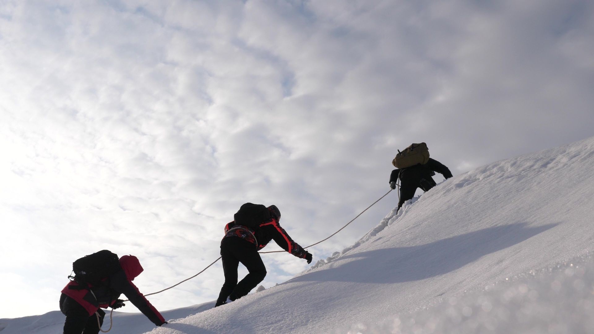 three Alpenists in winter climb rope on mountain. Travelers climb rope to their victory through snow uphill in strong wind. tourists in winter work together as team overcoming difficulties.